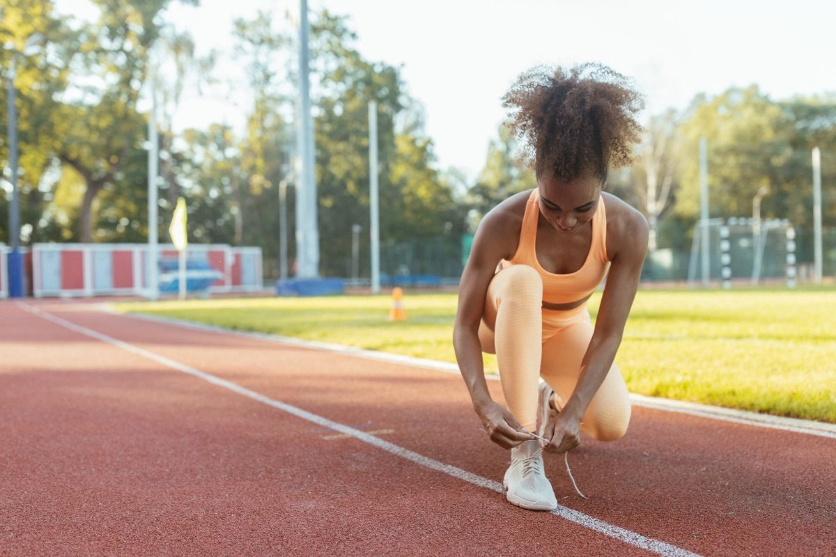 A runner tying her shoe on an outdoor track before a workout.